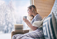 Frau trinkt im Winter auf Sofa Tee und liest Buch
