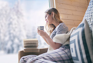Frau sitzt im Winter auf dem Sofa und trinkt Tee 